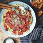 A plate of spaghetti topped with tomato sauce, fresh basil leaves, and grated cheese—served with a fork, spoon, garlic bread, and extra cheese on the side—is just one of the delicious meals you’ll find in Super Easy Pasta! from Simon & Schuster, the perfect choice for anyone seeking quick pasta dishes or easy recipes to enjoy any night of the week.
