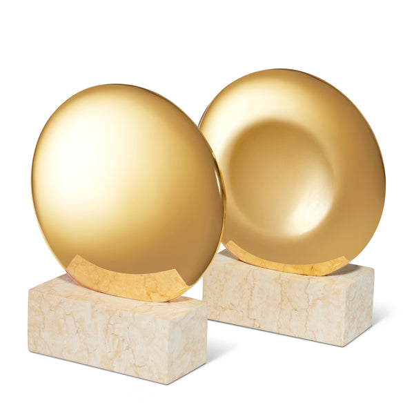 The AERIN Constantin Bookend Set by Aerin features round, gold-colored sculptures atop rectangular beige limestone plinths, reflecting mid-century design with timeless charm.