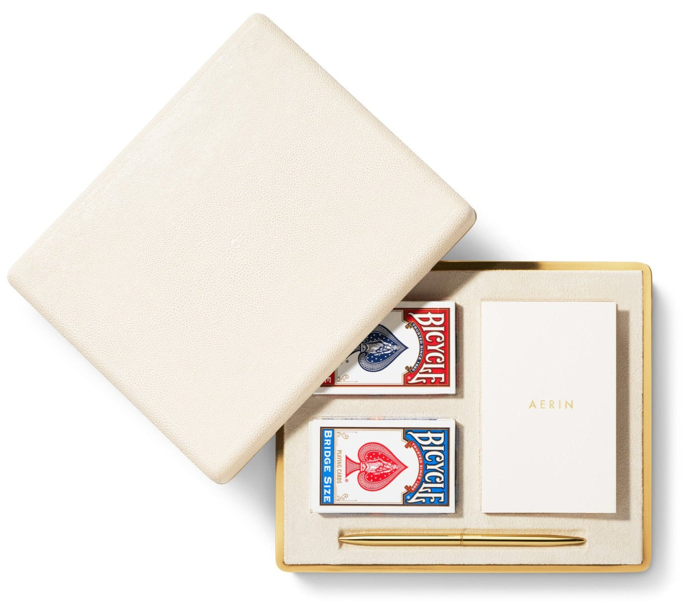 The Aerin Shagreen Bridge Set in cream features two Bicycle playing card decks, an "AERIN" notepad, and a gold pen—all in an embossed case for a refined luxury travel accessory.