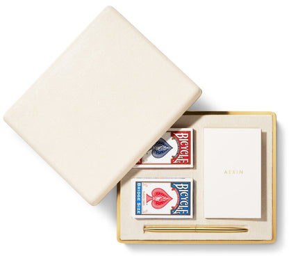 The Aerin Shagreen Bridge Set in cream features two Bicycle playing card decks, an "AERIN" notepad, and a gold pen—all in an embossed case for a refined luxury travel accessory.