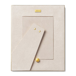 The Colette Cane Frame by AERIN is a beige rectangular picture frame with a cane-textured surface, gold accents, and "AERIN" on a gold plate at the top. The stand is extended.