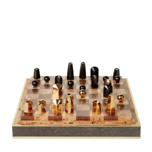 The Shagreen Chess Set Collection by Aerin features gold-plated geometric pieces on a brown and beige board, elegantly presented in a luxurious shagreen box.