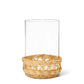 The Navona Rattan Hurricane Collection by Aerin features a clear cylindrical glass hurricane in a woven, light-toned rattan holder with a pedestal base, adding natural elegance to your décor.