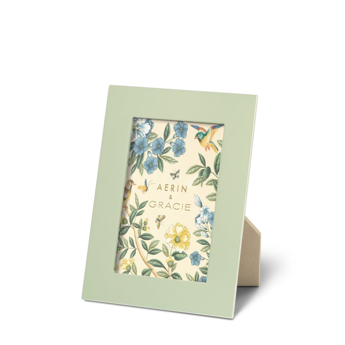 A frame from the AERIN x Gracie Heathcote Collection by Aerin features a green finish with a floral and hummingbird design insert, reminiscent of traditional interiors. It showcases the text "Aerin & Gracie" and stands upright with a beige easel back.