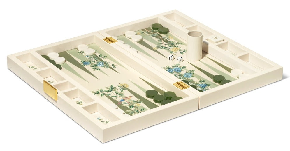 The AERIN x Gracie Heathcote Lacquer Backgammon Set features a Heathcote design with a floral motif board, white and green checkers, two dice, and dice shaker. It evokes elegant hand-painted wallpapers, blending artistry with classic gaming tradition.