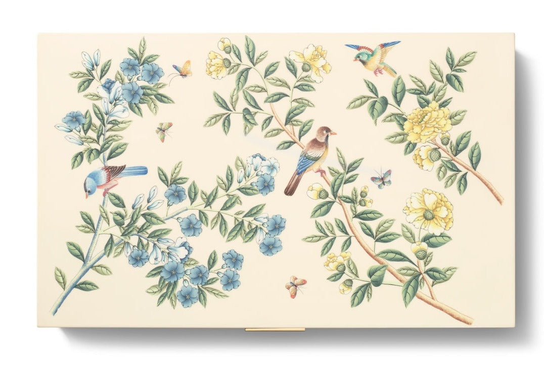 The AERIN x Gracie Heathcote Lacquer Backgammon Set features a Heathcote design with birds, butterflies, and blue and yellow flowers on branches against a cream background.