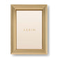 A gold rectangular photo holder from the Alessio Frame Collection by Aerin, this frame features a reeded design with layered ridges and displays a blank insert printed with "AERIN"—ideal for showcasing elegant photographs.