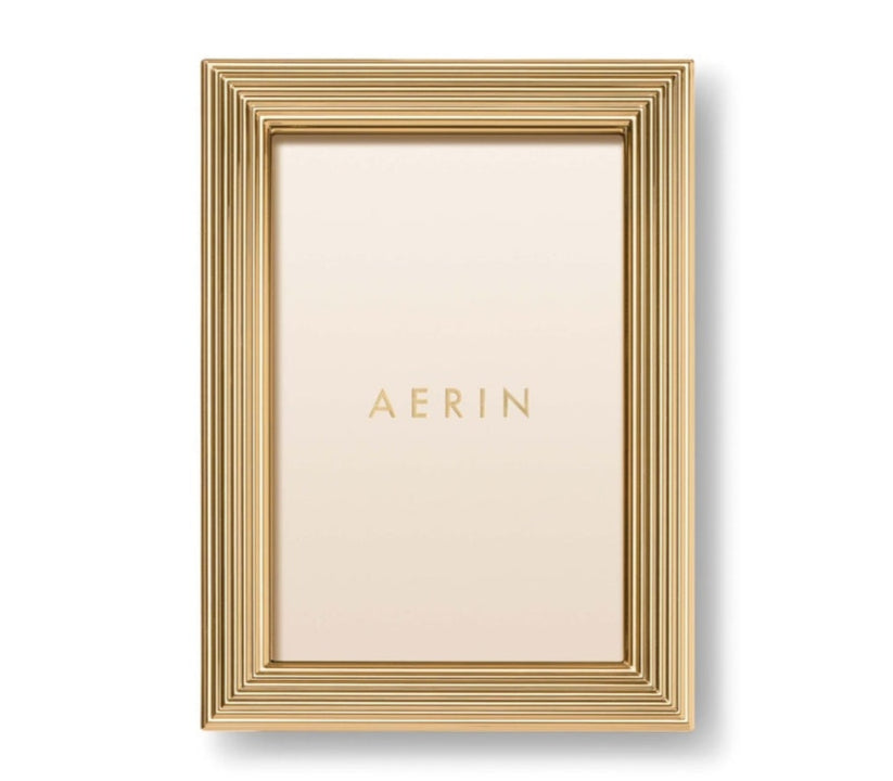 A gold rectangular photo holder from the Alessio Frame Collection by Aerin, this frame features a reeded design with layered ridges and displays a blank insert printed with "AERIN"—ideal for showcasing elegant photographs.