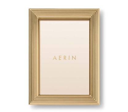 A gold rectangular photo holder from the Alessio Frame Collection by Aerin, this frame features a reeded design with layered ridges and displays a blank insert printed with "AERIN"—ideal for showcasing elegant photographs.