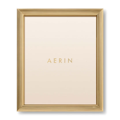 The Alessio Frame Collection by Aerin features a gold reeded rectangular design, with "AERIN" in gold on a cream background—ideal for elegantly displaying your favorite photos.