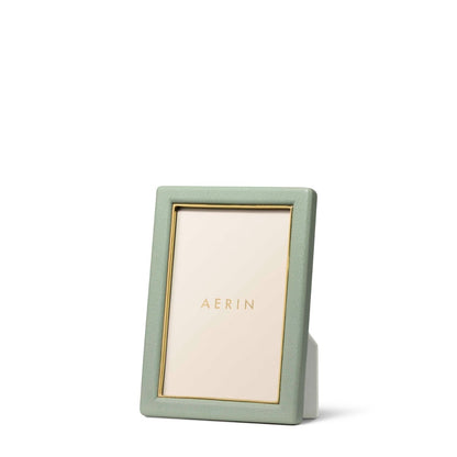 The Piero Leather Frame Collection by Aerin features a vertical green leather frame with gold accents and a gold inner border, displaying an "AERIN" placeholder card against a white background for an elegant touch.