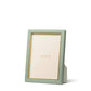 The Aerin Piero Leather Frame Collection features a green rectangular frame with gold detailing, displaying an "AERIN" card. This elegant piece stands upright on a white surface, bringing sophisticated style to any room.
