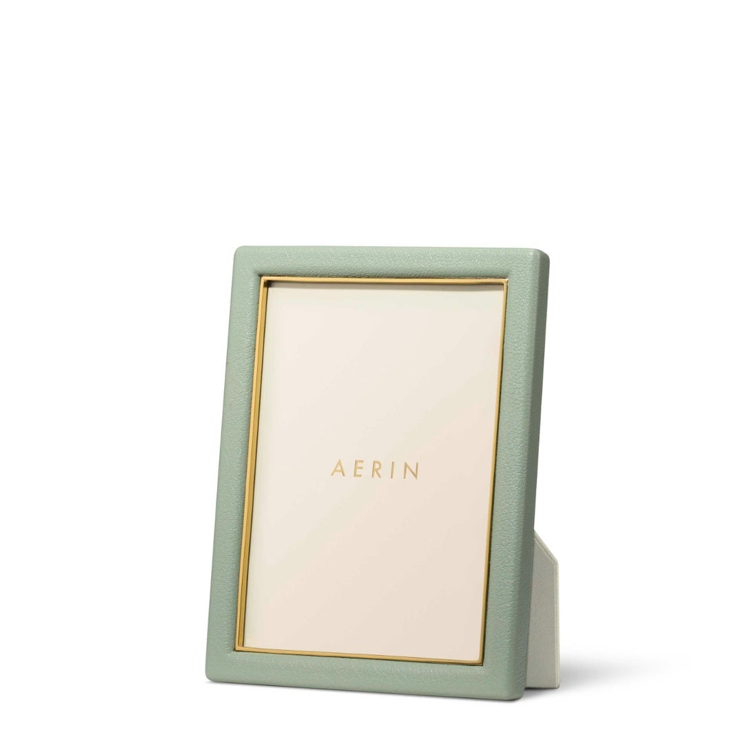 The Aerin Piero Leather Frame Collection features a green rectangular frame with gold detailing, displaying an "AERIN" card. This elegant piece stands upright on a white surface, bringing sophisticated style to any room.