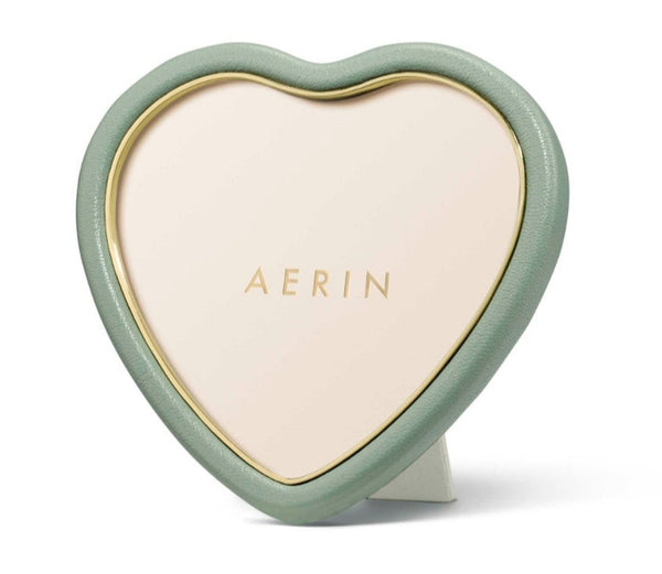 The AERIN Eucalyptus Piero Leather Heart Frame by Aerin is a heart-shaped photo frame featuring a green border and gold "AERIN" lettering on a beige background. It's an exquisite, sophisticated piece perfect for gifting.