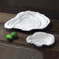 The Beatriz Ball Vida Ocean Oyster Bowl Collection features two white luxury melamine oyster-shaped dishes, placed on a rustic wooden surface with two whole limes—ideal for stylish indoor and outdoor entertaining.