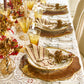 A formal dining table set with Kim Seybert Majorelle Napkin Set, gold-accented glasses, autumn-themed centerpieces, and layered plates on woven placemats.