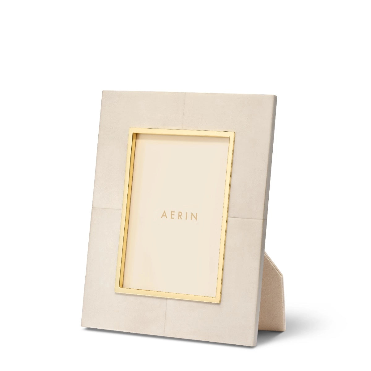 The Aerin Livio Parchment Frame Collection features a beige rectangular leather frame with gold trim and subtle brass detailing around the inner edge, designed to stand upright with a visible rear support.
