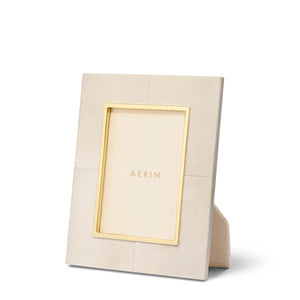 The Aerin Livio Parchment Frame Collection features a beige rectangular leather frame with gold trim and subtle brass detailing around the inner edge, designed to stand upright with a visible rear support.