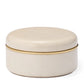 The Livio Parchment Coaster Set by Aerin features a round, cream-colored box with a smooth lid, thin gold band, and subtle Art Deco-inspired brass detailing separating the lid from the base.