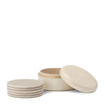 The Aerin Livio Parchment Coaster Set includes five round beige leather coasters with brass accents and a matching lidded holder, shown with four stacked beside the open container.