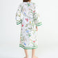 A woman seen from behind wearing an Yves Delorme x Laurence Tavernier Botanic Dressing Gown in white with a floral print and green striped trim.