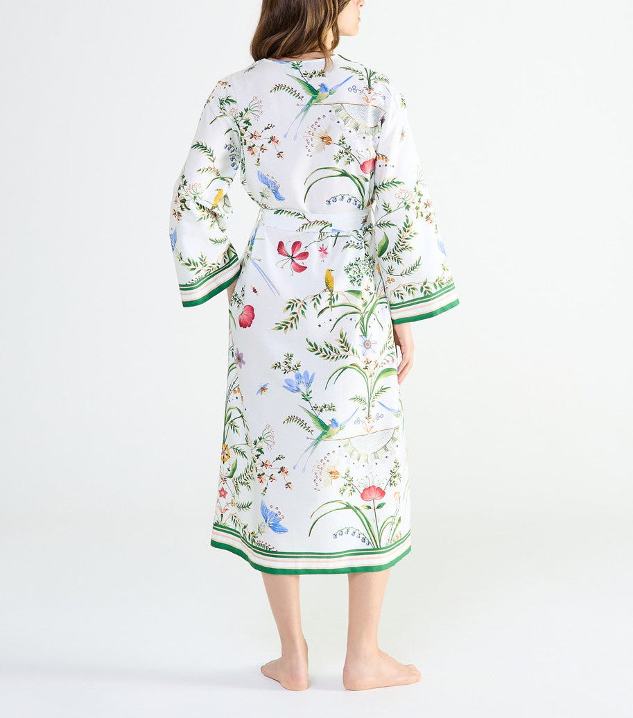 A woman seen from behind wearing an Yves Delorme x Laurence Tavernier Botanic Dressing Gown in white with a floral print and green striped trim.
