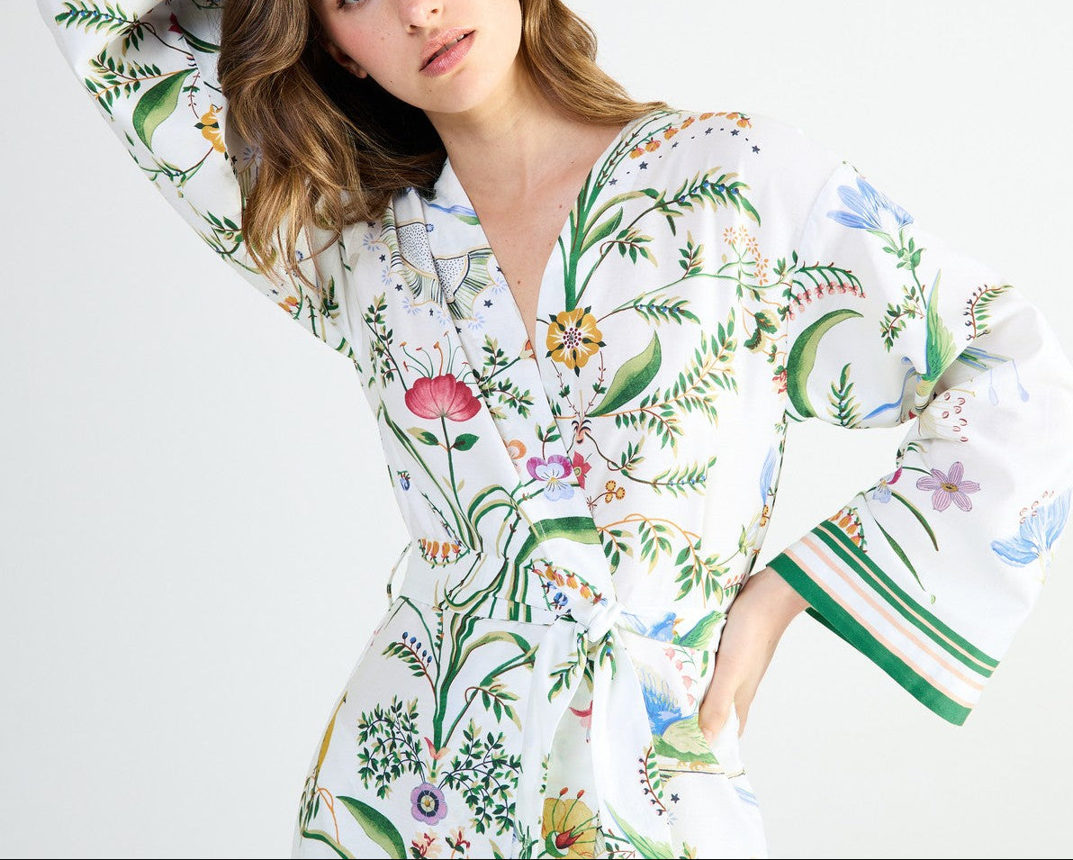 Yves Delorme x Laurence Tavernier Botanic Dressing Gown in white cotton sateen with a colorful botanical print, green-striped cuffs, and a wrap-style tie waist.