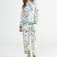 A person wearing Yves Delorme x Laurence Tavernier Botanic Pajamas featuring a colorful floral and bird design with green trim at the cuffs and hem.