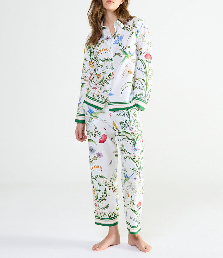 A person wearing Yves Delorme x Laurence Tavernier Botanic Pajamas featuring a colorful floral and bird design with green trim at the cuffs and hem.