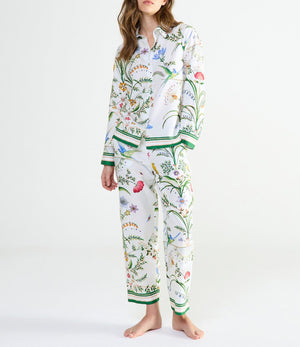 A person wearing Yves Delorme x Laurence Tavernier Botanic Pajamas featuring a colorful floral and bird design with green trim at the cuffs and hem.