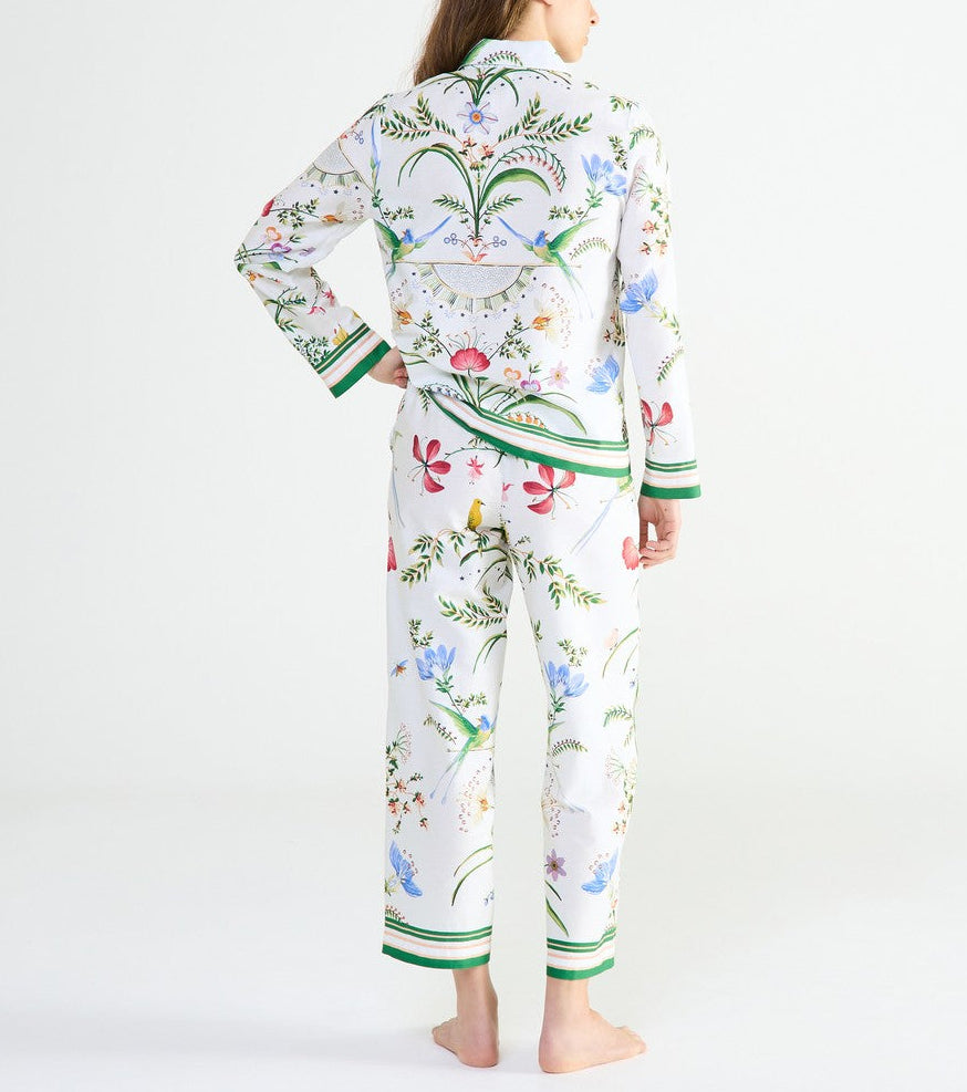 A person wearing Yves Delorme x Laurence Tavernier Botanic Pajamas featuring a colorful bird print and green striped cuffs.