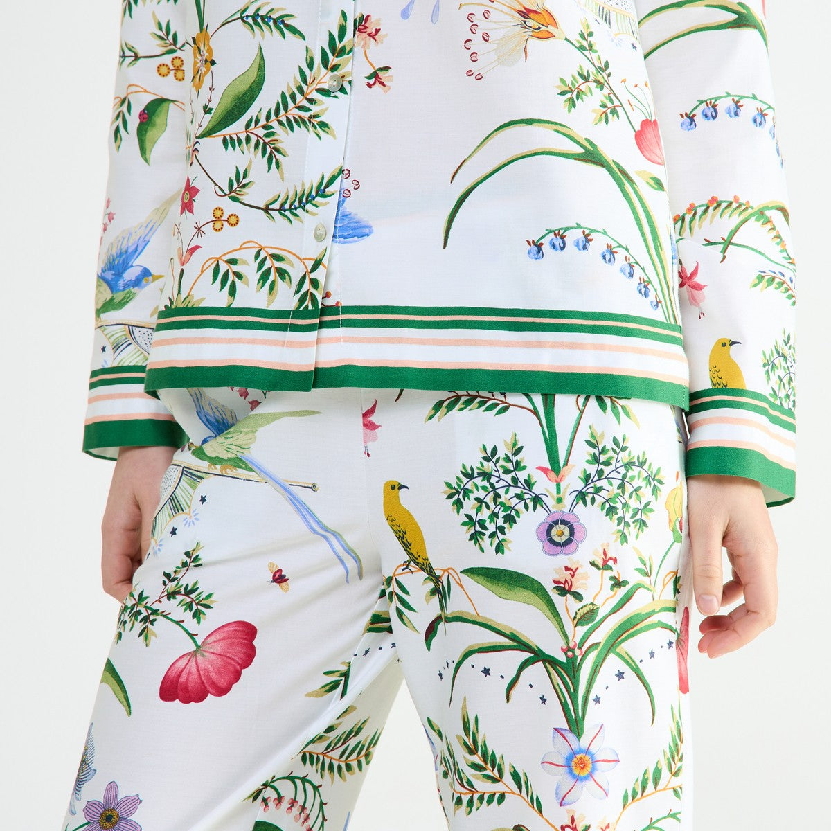 A person wearing white Yves Delorme x Laurence Tavernier Botanic Pajamas featuring a colorful botanical floral print of birds and flowers.