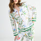 Yves Delorme x Laurence Tavernier Botanic pajamas consisting of a long-sleeved button-down top and matching pants in a floral print with colorful flowers, birds, and insects on a white background.
