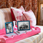 On a striped sofa, the Addison Ross Scalloped Watermelon Pink Lacquer Tray holds two framed photos, a small glass vase, and two books; patterned pillows and a curtain appear in the background.