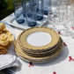 Juliska’s Bamboo Caning Melamine Dinnerware Collection is stacked on a white tablecloth with red embroidery, paired with yellow napkins, clear wine glasses, and blue tumblers for a vibrant tablescape.