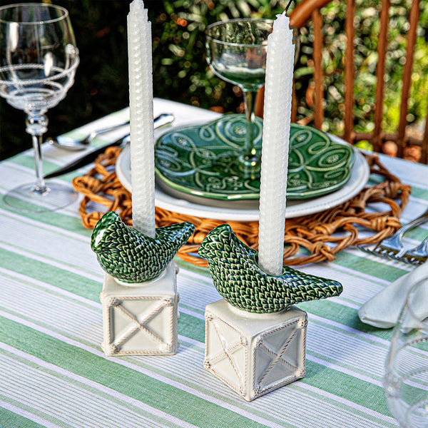 The Berry & Thread Bird Topiary Candlestick Set by Juliska features two white candles in green songbird-shaped holders, displayed on a striped tablecloth amidst glassware and green plates for a fresh spring tablescape.