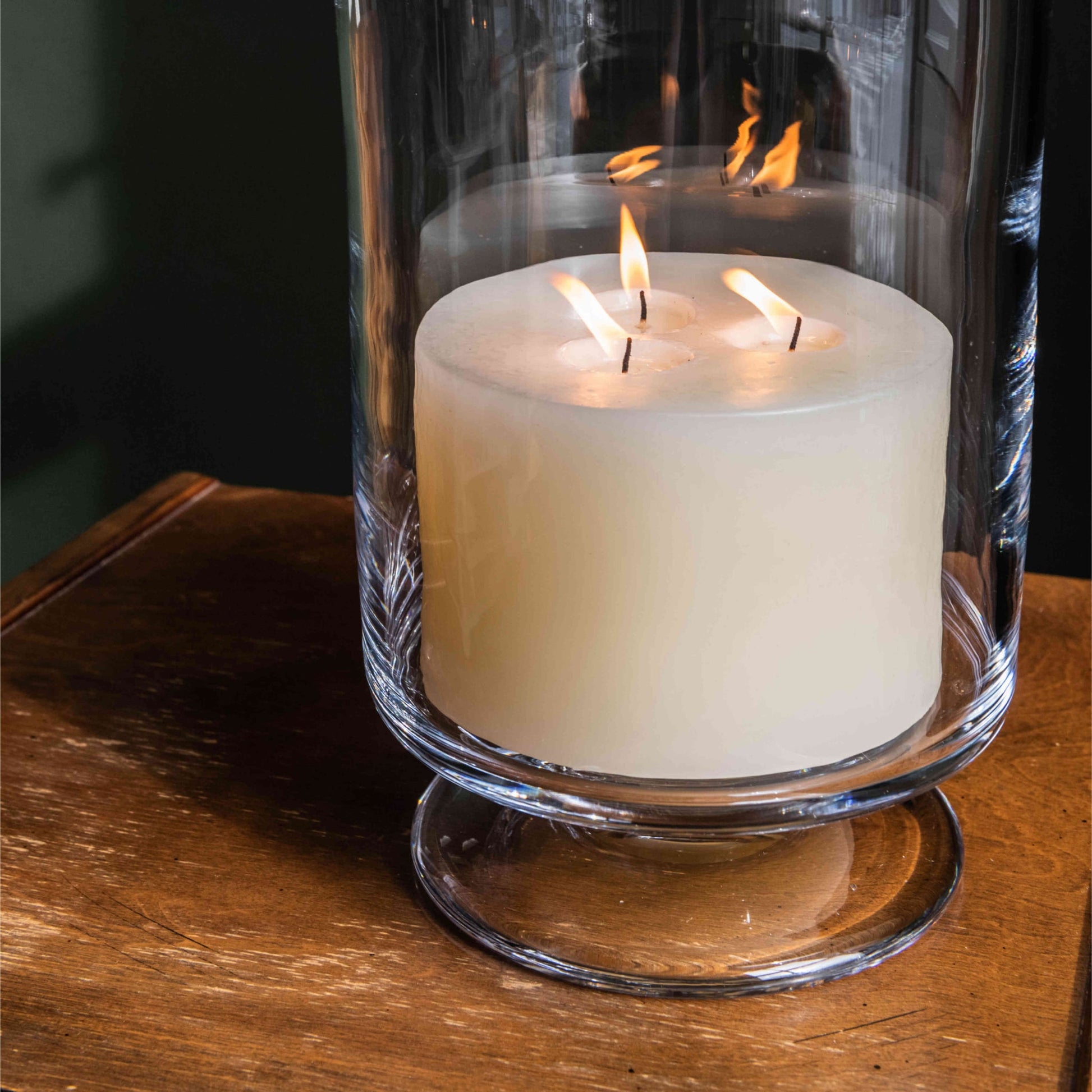 The Simon Pearce Ivory Candle Collection features a large, three-wick artisan candle in a clear glass holder, adding warmth and elegance to your home décor.