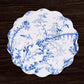 A Beatriz Ball VIDA Chinoiserie Reversible Round Placemat in blue and white holds a white plate with blue oriental-style designs, beautifully displayed on a dark wooden surface.