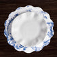 A white porcelain plate with a blue floral design rests on a matching scalloped charger, accented by Beatriz Ball’s VIDA Chinoiserie Reversible Round Placemats in blue and white on a dark wood table.