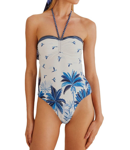 Person wearing a Farm Rio Dream Sky One Piece by Farm Rio with blue tropical palm tree and bird patterns, elegantly paired with a matching sarong.