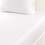A close-up of a white pillow and fitted sheet from the Adagio Blanc Bedding Collection by Yves Delorme, both in luxurious 500 thread count cotton sateen, with the pillow showcasing elegant quilted etoile embroidery.