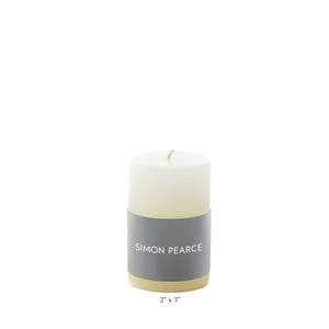 The Simon Pearce Ivory Candle Collection features a white pillar candle with a gray label, measuring 2" x 3". This artisan piece adds understated elegance to your home decor.