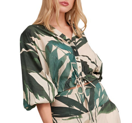 A woman wearing the Cara Cara Perrin Top, an airy cotton voile blouse by Cara Cara in beige with a green leaf pattern, featuring buttons, puffy sleeves, and a subtle oversized silhouette.