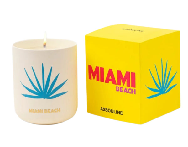 Next to a bright yellow box labeled "Miami Beach Assouline," the white jar features a lit wick and blue palm design, offering the summer fragrance of sandalwood and lively beach parties. It's called Travel Candle Miami by Assouline.