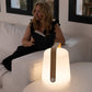 A woman sits on a white sofa reading, while a Fermob Bamboo Balad 10" Lamp with a wooden handle casts a warm, portable glow on the nearby table.