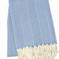 The Nantucket Herringbone Throw Collection by A Soft Idea features blue and white stripes with diagonal lines and hand-knotted fringe tassels on one end.