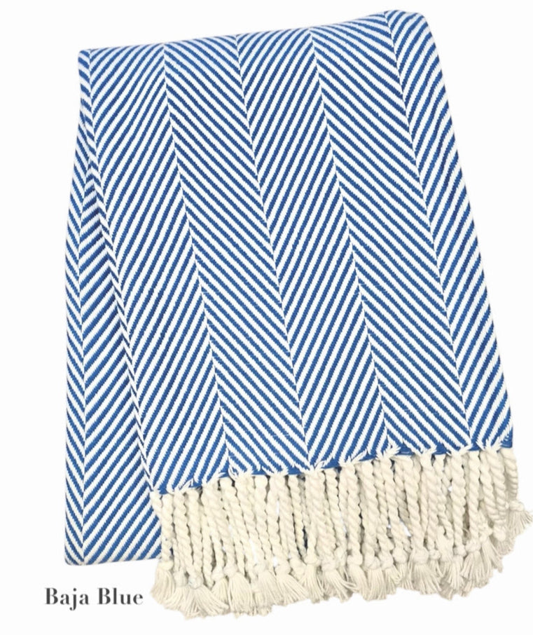 The Nantucket Herringbone Throw Collection by A Soft Idea features blue and white stripes with diagonal lines and hand-knotted fringe tassels on one end.