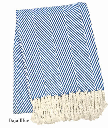 The Nantucket Herringbone Throw Collection by A Soft Idea features blue and white stripes with diagonal lines and hand-knotted fringe tassels on one end.