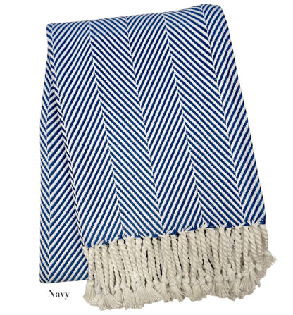 The Nantucket Herringbone Throw Collection by A Soft Idea features a folded navy and white throw with hand-knotted fringe, classic herringbone pattern, and soft cotton craftsmanship.