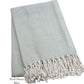 A folded light blue and white throw from the Nantucket Herringbone Throw Collection by A Soft Idea, featuring hand knotted fringe, labeled "Pool Shore Blue.